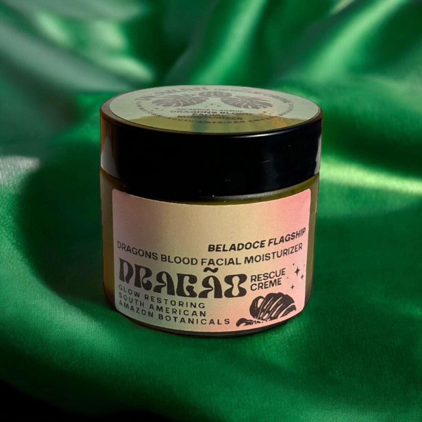 The Beladoce Botanicals Dragão Rescue Creme jar with the lid slightly open, showcasing the creamy, buttery texture of the winter reserve formula. A wooden spatula lies beside it, ready for application. The backdrop includes a hint of greenery, reinforcing its Amazonian origins.